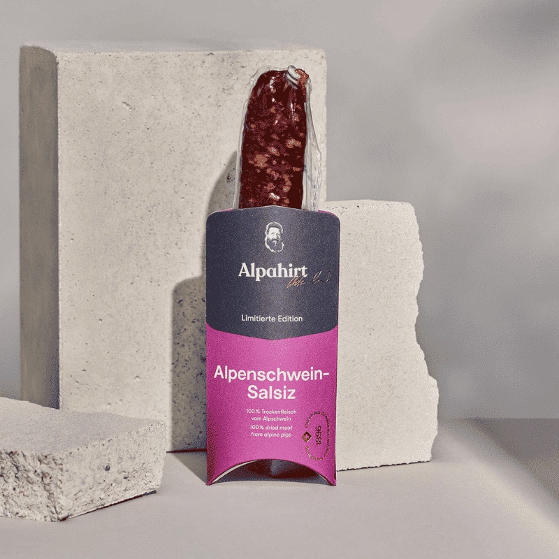 Alpenschweinsalsiz vor Steinen aufgestellt in ganzer Verpackung