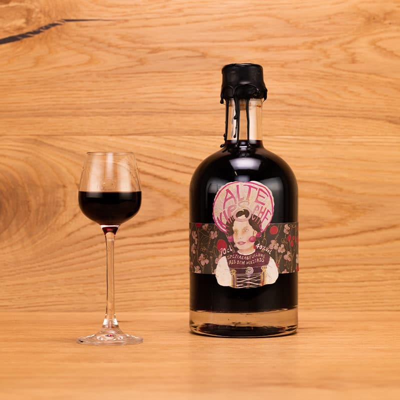 Alte Kirsche Holzfassbrand in kleiner dekorativer Flasche mit hübscher Etikette und Wachsverschluss und eingeschenktem Schnapsglas