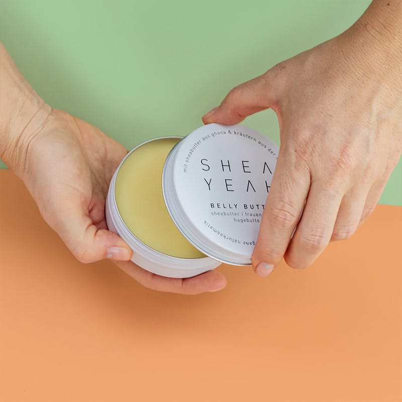 Zwei Hände öffnen die Belly Butter