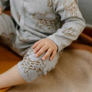 Kleiner Junge in grauen Body mit senfgelben Leoparden und Pflanzen sitz auf einer Decke.