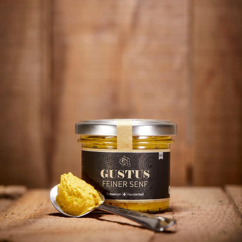 Gustus feiner Senf als Glas davor ein Löffel mit etwas Senf