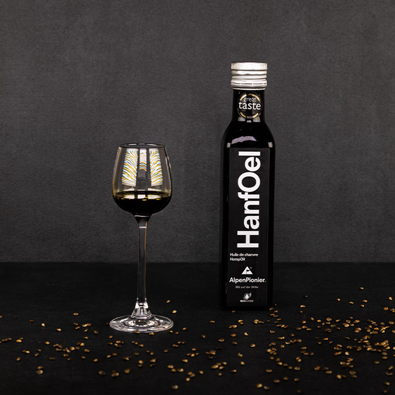 Flasche mit Glas gefüllt mit dunkelgrünem Hanfoel daneben