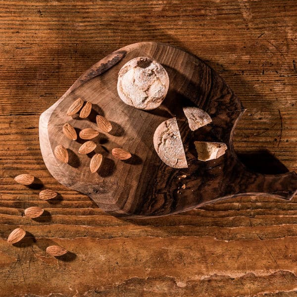 Amaretti aufgeschnitten auf Holzbrett mit Mandeln die daneben liegen