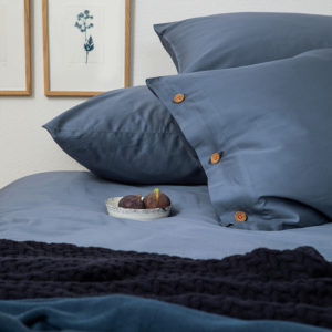 Auschnitt eines Schlafzimmers mit taubenblauer Bettwäsche und Bildern an der Wand