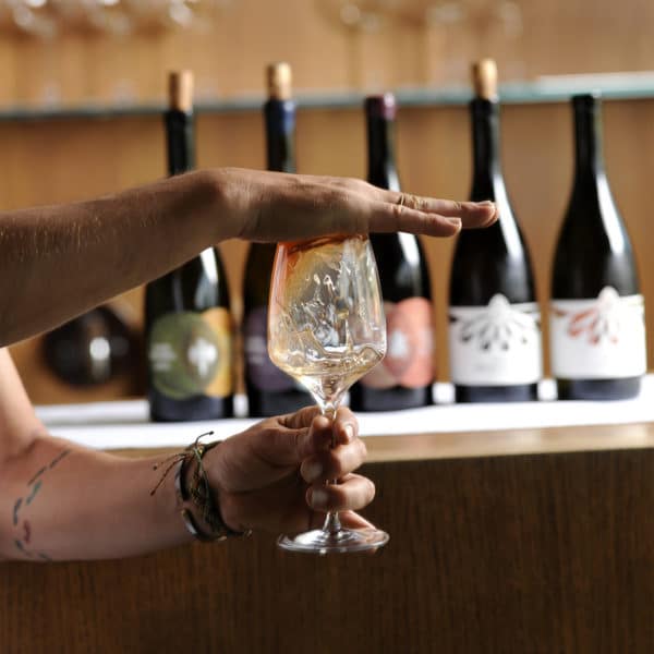 Eine Hand auf einem Glas Wein im Hintergrund stehen Weine von Ploder Rosenberg