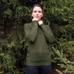 Frau steht vor einer grünen Tanne und trägt den olivgrünen Unisex Pullover von ROTAUF. Sie trägt eine schwarze Hose und schulterlange dunkelbraune Haare