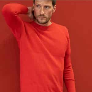 Mann steht vor einer roten Wand und trägt den roten Unisex Pullover von ROTAUF.