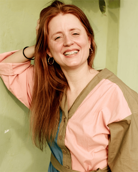 Sandra von SHEA YEAH in farbigem Oberteil, fasst sich mit der rechten Hand in die Haare und lacht