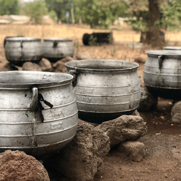 Metalltöpfe aneinandergereiht, die auf Steinen liegen. Mit Shea Masse gefüllt