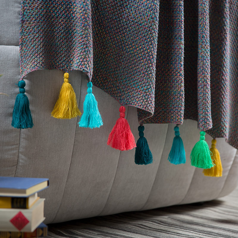 Strickdecke mit farbigen Zotteln hängt vom Sofarand herunter