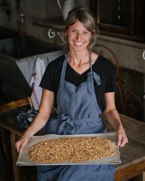 Teammitglied von the tiny factory mit frisch geröstetem Granola auf dem Blech in den Händen